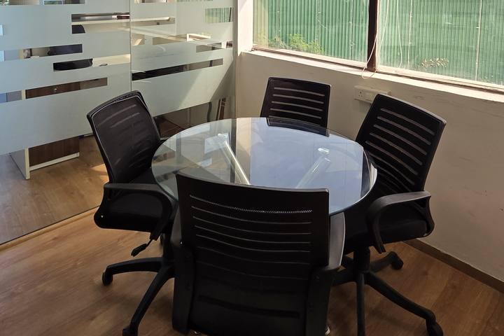 Round glass-top meeting table with black chairs beside a frosted-glass partition and a large window at Livance NH-8, Gurgaon