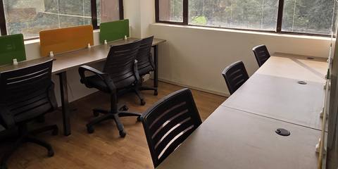 Desks with black office chairs on a wooden floor beside large windows at Livance NH-8