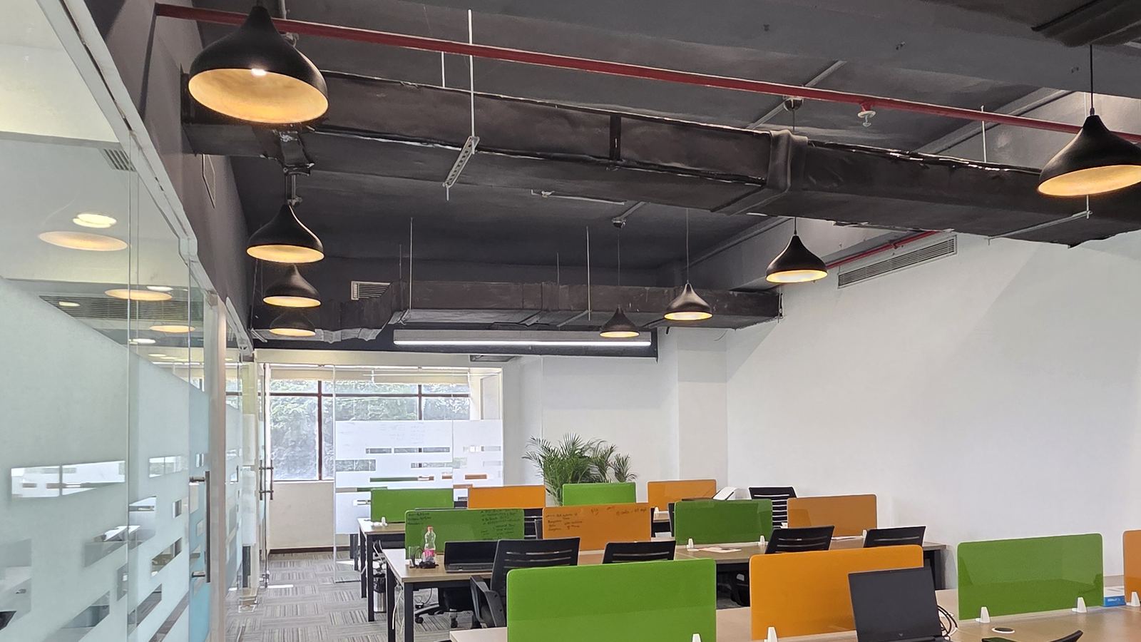Open workspace at Livance NH-8 with green and orange desk dividers, black pendant lamps and glass partitions